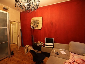 торшер в стиле хай-тек, тумбочка с телевизором и разложенный диван с постельным у красной стены спальной комнаты разноплановой трехкомнатной квартиры