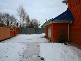 невысокая елочка в снегу на просторном участке с расчищенными дорожками кирпичного двухэтажного гостевого дома с придорожным кафе