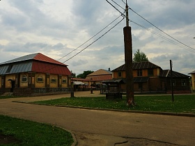 деревянный колодец под треугольной крышей, высокий столб с линией электропередач и фонарный столб на зеленой поляне в черте старого городка для съемок кино