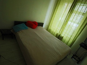 обычная кровать с деревянной спинкой с разноцветными подушками в спальне съемной квартиры