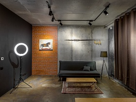 деревянный журнальный стол на цветном ковре у серого мягкого дивана на бетонном полу в современной студии в серых тонах