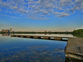 перистые белые облака на голубом небе над водной гладью живописного озера с длинным деревянным пирсом