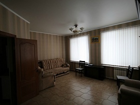 картина над темной тумбочкой, два стула, бежевый мягкий диван и кресла в просторной гостиной пустого двухэтажного дома под съем