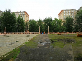 придомовая территория сталинского здания наполовину покрытая плиткой за окрашенным невысоким бетонным резным забором