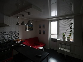 подвесные люстры в стиле хай-тек над черным обеденным столом вишневой кухни с диваном под вишневым чехлом, круглыми белыми стульями на черном полу квартиры на первом этаже