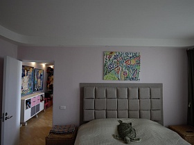цветная картина на розовой стене над большой кроватью с бежевым покрывалом, прикроватные тумбочки в спальной комнате стильной трехкомнатной квартиры