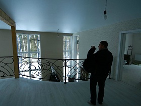 светлый деревянный пол лестничной площадки с кованными фигурными перилами и открытой дверью в соседнюю комнату недостроенного элитного дома