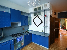 мебельная стенка с синей поверхностью закрытых шкафов, встроенной газовой плитой , открытыми полками и барной фурнитурой над барным столом светлой кухни квартиры художника
