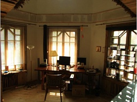 стеллаж с открытыми полками и длинный полированный стол у большого окна рабочего кабинета