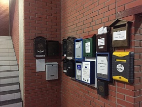 разнообразные почтовые ящики на кирпичной стене на первом этаже в подъезде жилого дома с лестничными пролетами