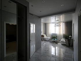 вид из прихожей на светлую гостиную с белой мебелью, белыми вертикальными жалюзи на окне и серыми вазонами с комнатными цветами