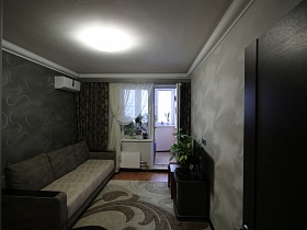 большой диван, телевизор на тумбе, большой светлый ковер на полу гостиной, выдержанной в двух цветах - белого с серым современной дизайнерской трешки в новостройках Измайлово
