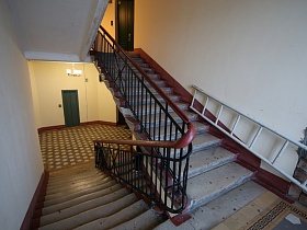 просторная лестничная площадка с бежево коричневой плиткой на полу у дверей лифта и квартир с высоты ступеней лестницы в подъезде дома на Новослободской