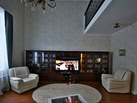 черные перила второго этажа в просторной светлой гостиной с белой мягкой мебелью и стенкой современного кирпичного дома