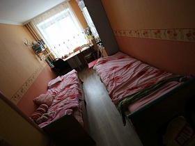 две деревянные кровати в узкой спальне с бежево розовыми стенами квартиры в областном квартале