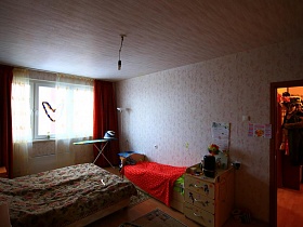 рядом с кроватью у стены стоит детская кровать с комодиком в спальной комнате нового жильяпо программе реновации