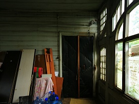 захламленная веранда с деревянными салатовыми стенами и обитой черной дверью деревянного двухэтажного дома в старом Ногинске