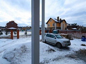 машина во дворе со снегом элитного недостроенного дома , окруженного металлическим решетчатым забором с кирпичными колоннами