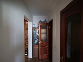 помпа и бутыля для воды на поверхности шкафа с посудой на полках у белой стены коридора с коричневыми дверьми со стеклянными вставками в соседние комнаты типичной просторной квартиры