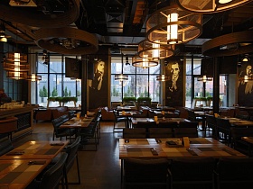 круглые абажуры светильников над индивидуальными столиками в помещении уютного крафтового ресторана с большими окнами