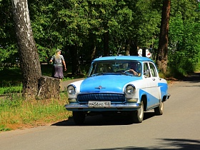 бело голубая ретро машина на проезжей части дороги вдоль густого зеленого парка при гостинице "Дубна" СССР