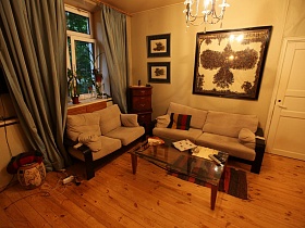 необычные картины на стене над мягким бежевым диваном и коричневым комодом в зонированной гостиной с серыми шторами на окне разноплановой трехкомнатной квартиры