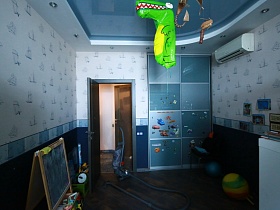 голубой шкаф для одежды с разноцветными квадратами на дверцах, игрушки на полу, мольберт в детской комнате с дизайнерским ремонтом молодежной квартиры в современном мегаполисе