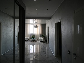 высокий шкаф-купе с зеркальными дверцами в коридоре современной лаконичной трехкомнатной квартиры с серыми стенами и квадратной плиткой под мрамор на полу