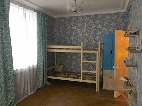 бело голубой шкаф для одежды, светлая двухэтажная кровать с матрасами и деревянной лестницей у голубой стены спальной комнаты с люстрой на белом потолке