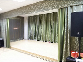 большие черные колонки у сцены с зелеными шторами и зеленым занавесом в актовом зале сельской школы