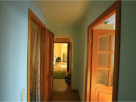 нежно голубые стены длинного коридора с арочным дверным проемом и открытыми дверьми в комнаты евро квартиры с видом на парк и Москву