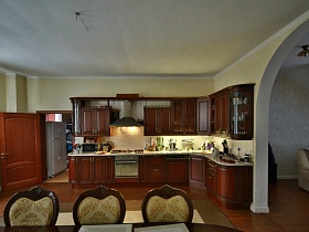 коричневая угловая кухонная стенка в светлой просторной гостиной с двухцветным ковром кирпичного современного дома
