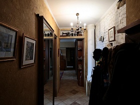 картины на стене, настенная вешалка с одеждой, люстра, стилизованная под свечи в длинном коридоре трехкомнатной квартиры времен СССР