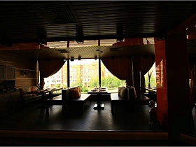 разноцветные мягкие квадратные подушки на коричневых диванах у сервированных столиков в ораньжевом зале с тяжелыми шторами на больших окнах евро ресторана