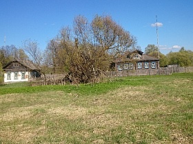 деревянный дом за забором и заброшенный с побеленными стенами без ограды по соседству в старой деревне Троица
