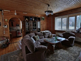 люстра с белыми круглыми плафонами над журнальным столиком и серой мягкой мебелью с подушками в центре гостиной уютной деревянной загородной дачи