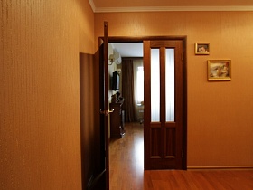 коричневые шторы на окнах, телевизор над камином в гостиной через открытые двери коридора трехкомнатной квартиры с детской комнатой