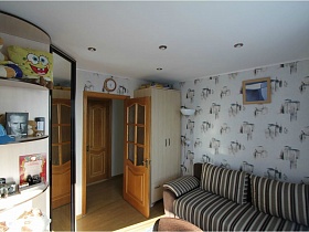картина над полосатым диваном с подушками, бежевый шкаф в углу за открытой дверью в юношескую комнату евро квартиры с видом на Москву и парк