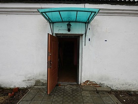 уличный фонарь на белой стене сельского клуба над входной дверью под бирюзовым навесом с площадкой, выложенной квадратной плиткой