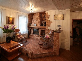 два кресло-качалки в отдельной зоне отдыха с плиткой, стойкой и декорированным камином под дикий камень в гостиной семейной уютной классической дачи