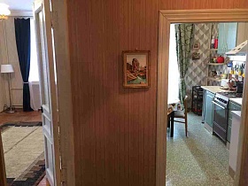 картина в рамке на стене с полосатыми коричнево-сиреневыми обоями и открытыми дверьми в светлую гостиную и зеленую кухню кв 27
