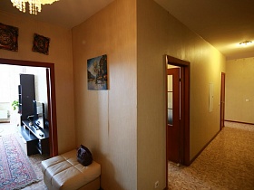 дамская сумочка на белом мягком пуфике у стены с картиной в большом светлом коридоре современной трехкомнатной квартиры в Химках