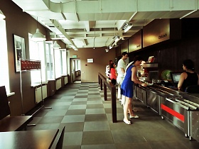 посетители столовой бизнес центра  с готовыми блюдами на разносах на линии раздачи у кассы