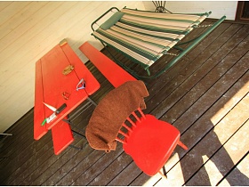 красный стул с полотенцем у длинного стола со скамейеками, полосатая раскладушка на коричневом полу деревянной постройки дачи работника кино