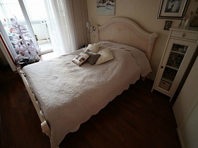 кровать с белым покрывалом, подушками и мебель пастельных тонов в светлой спальне современной трешки