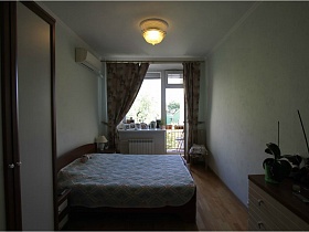 светлое стеганное покрывало на большой кровати в спальне с выходом на балкон в простой квартире на Садовом