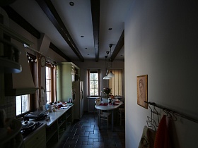 салатовая мебельная стенка,белый двухдверный холодильник, обеденный стол на полу светлой кухни загородного дома с сказочном стиле