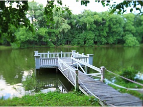 деревянный мостик на романтическую белую площадку с резными перилами в воде пруда