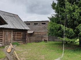 жилой дом и хозяйственные постройки из сруб дерева на большом дворе с деревянным козлом, деревянными скамейками на зеленой траве в деревне