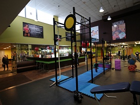 гимнастическая дорожка, силовые тренажеры, диван и барные стулья у барной стойки в общем просторном зале простого фитнеса
